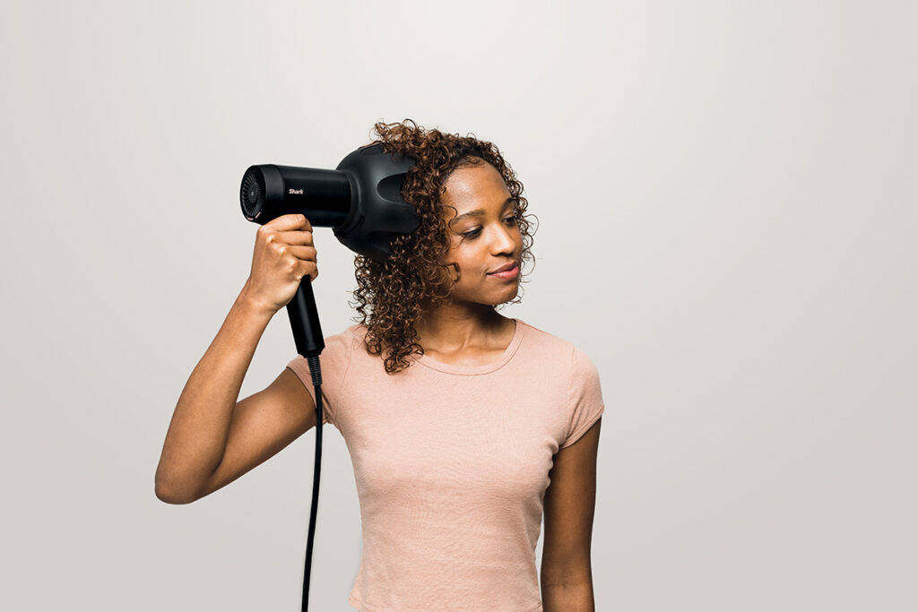 A woman using the diffuser nozzle on her Shark hairdryer to enhance her natural curls